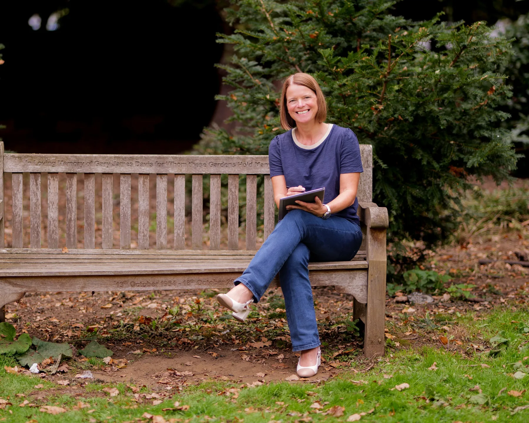 Niki Corbishley, leadership coach, sitting on a park bench with a notebook