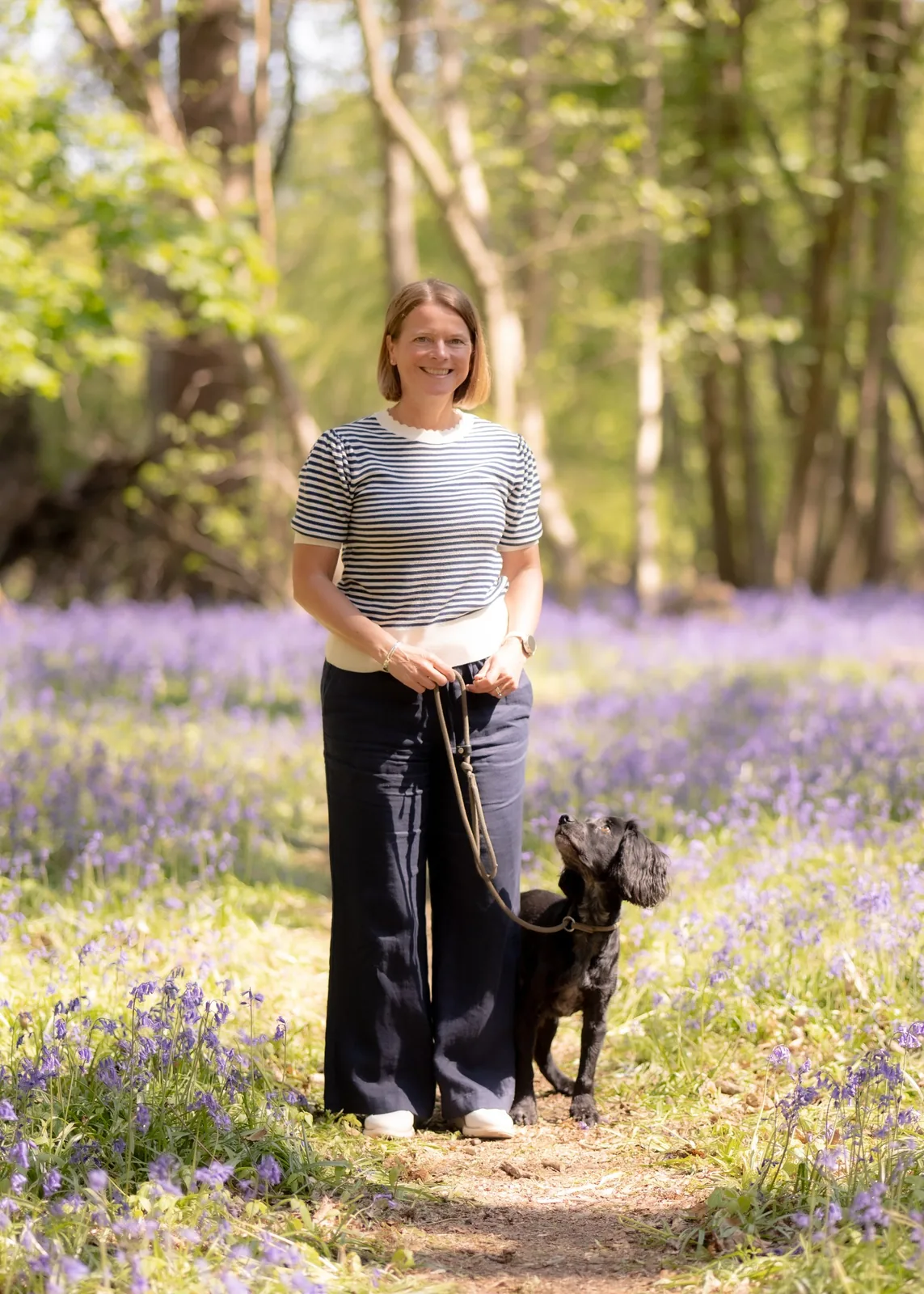 Niki Corbishley, leadership coach, standing in a bluebell wood with her cocker spaniel Oakley