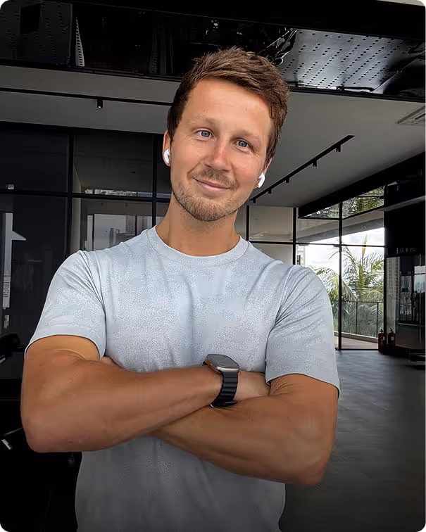 A confident Joshua Stephenson, personal trainer, poses with arms crossed in front of a large window, showcasing his expertise.