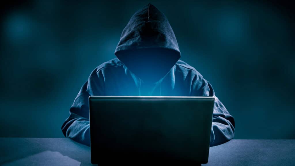 Hooded man in front of a laptop committing identity theft