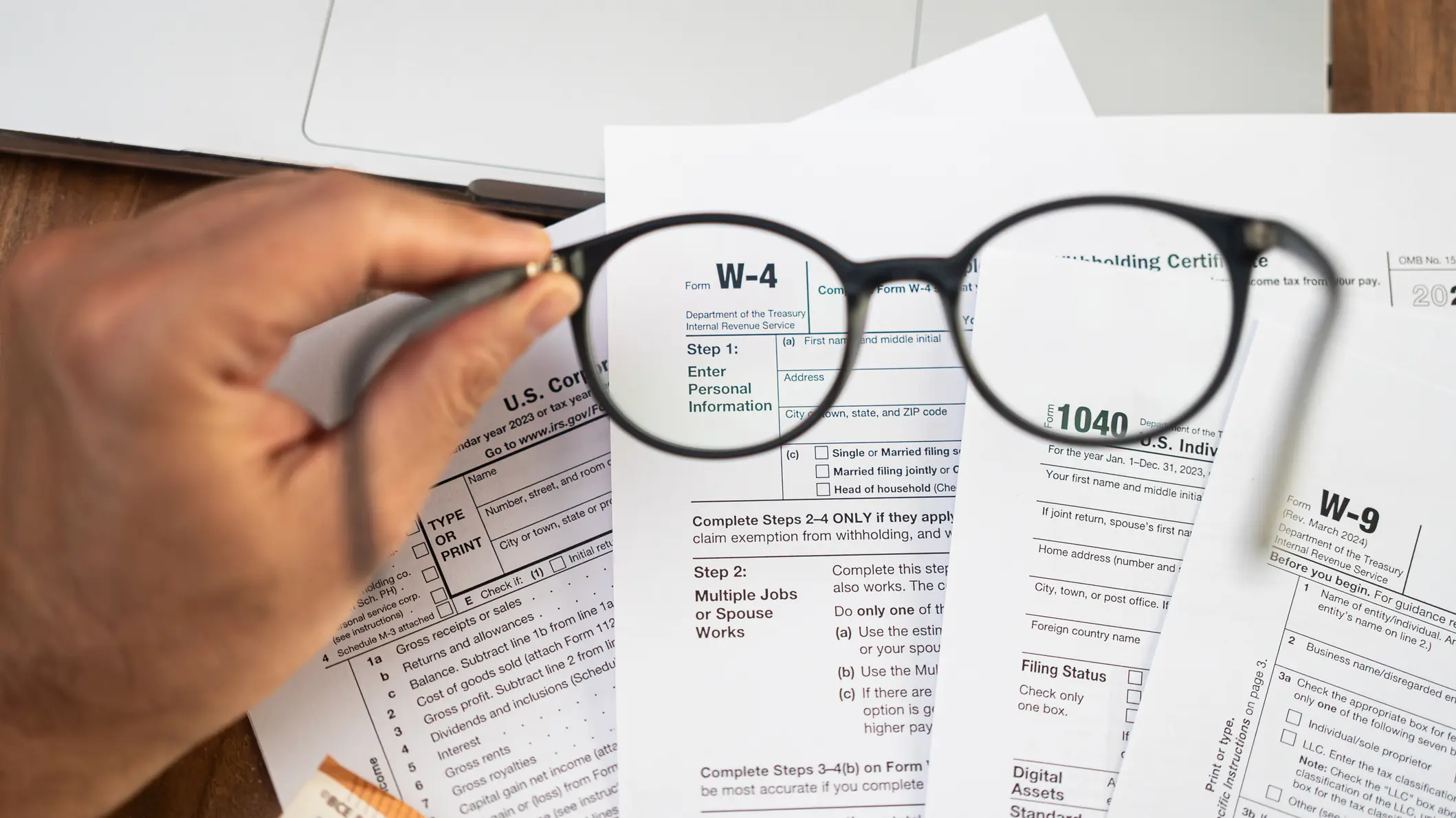 A hand holding eyeglasses above a stack of tax documents, suggesting close review and financial scrutiny.