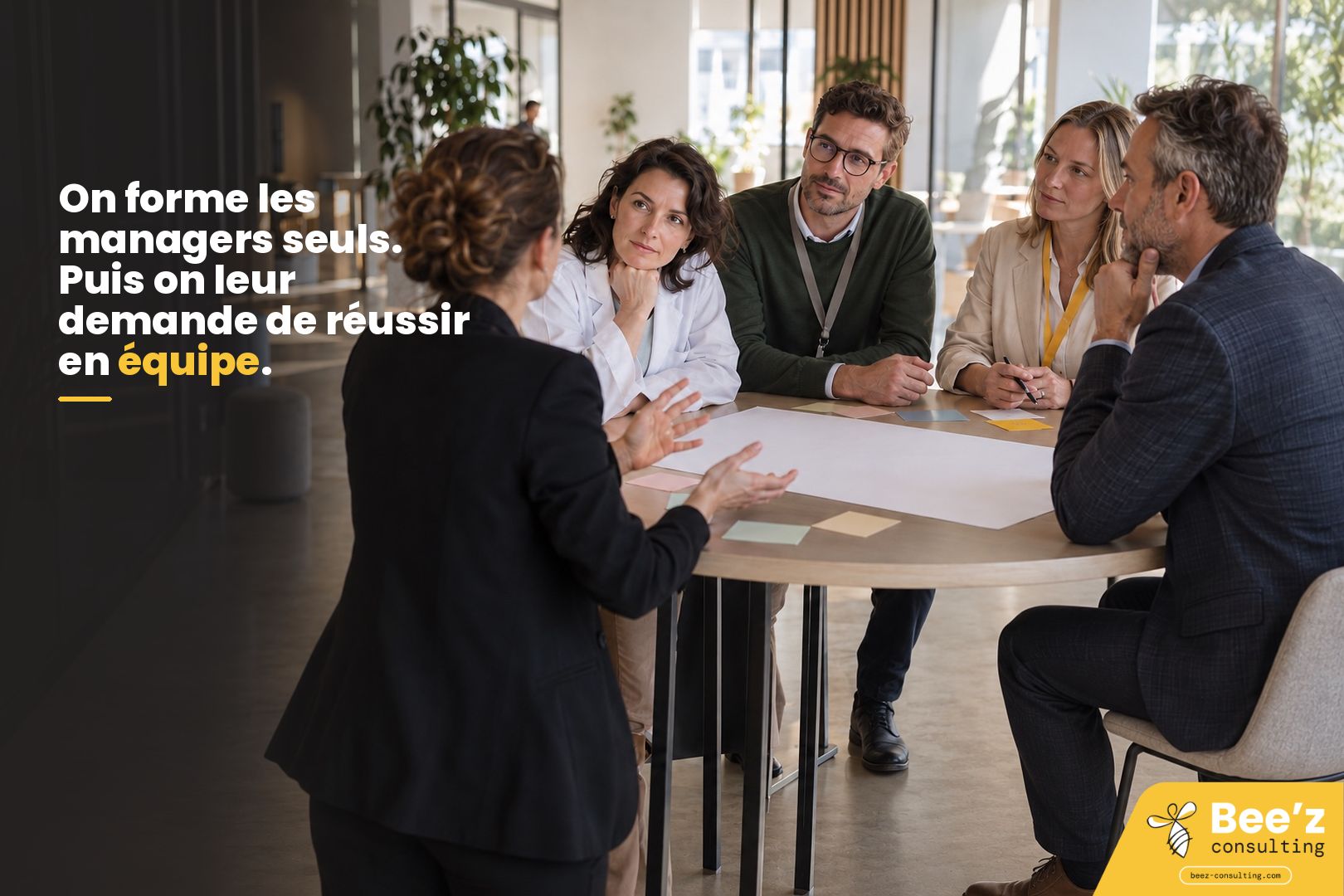 Une femme de dos s’adresse à quatre collègues attentifs, dont une en blouse blanche, autour d’une table couverte de post-it.