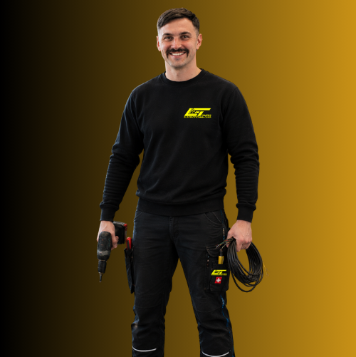 Nazmi Kodraliu, Geselle bei der Elektrotechnik Jung GmbH, trägt dunkle Arbeitskleidung und steht mit freundlichem Blick vor einem gold-schwarzen Hintergrund.