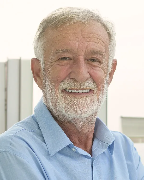 Smiling elderly man with white beard and hair wearing a light blue collared shirt.