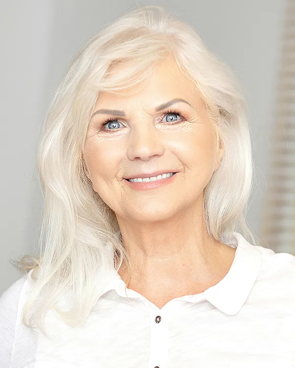 Smiling elderly woman with long white hair and blue eyes wearing a white collared shirt.