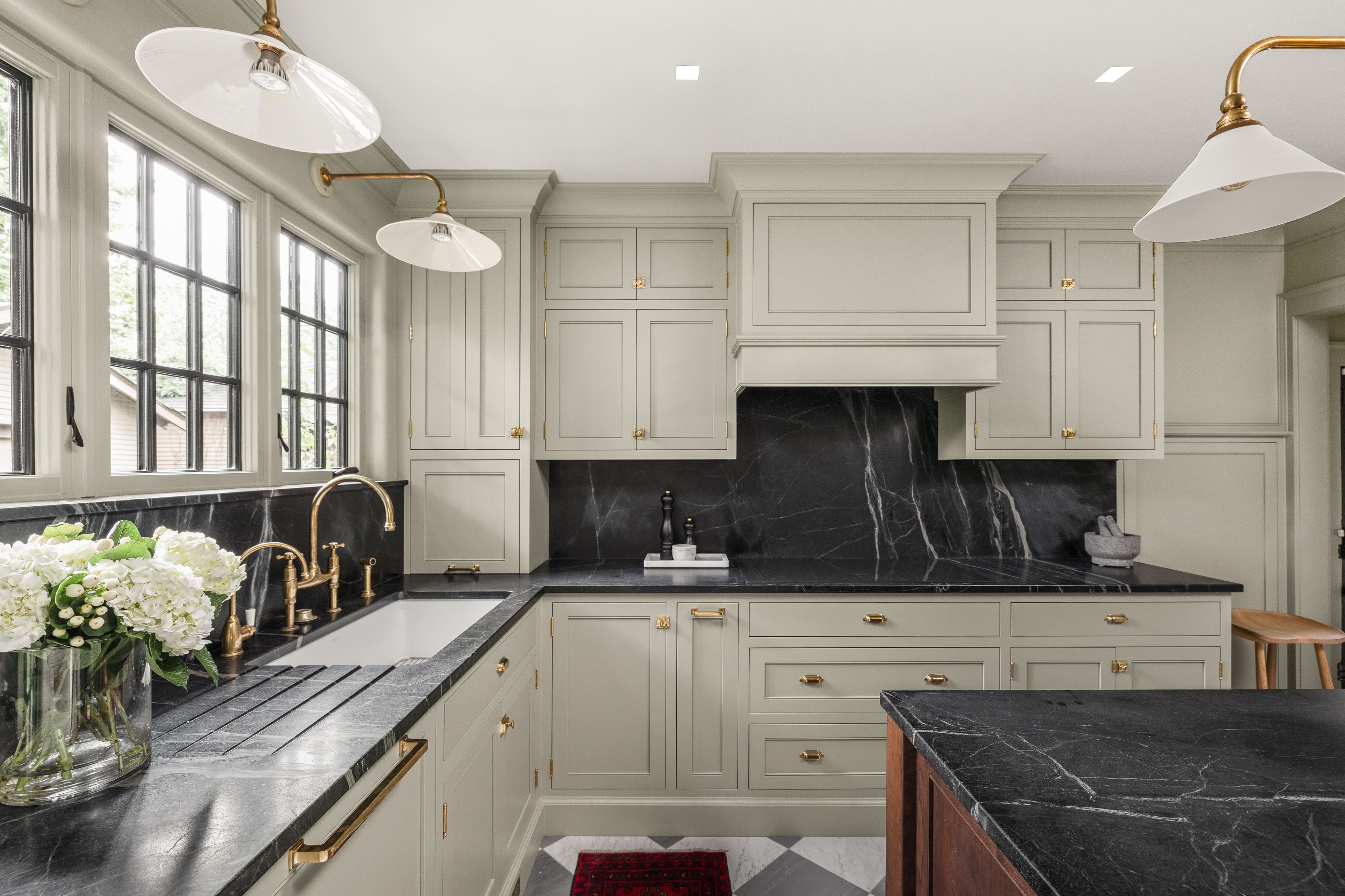Remodeled kitchen with custom made light green cabinets, black stone countertops, with brass fixtures and hardware