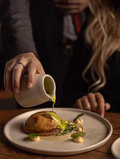 Server pouring sauce over steak for guests prepared in Neighbourhood’s award-winning steakhouse setting in County Kildare.