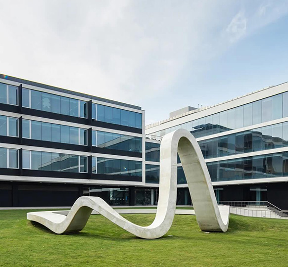 Escultura abstrata curva de betão sobre a relva em frente ao edifício de escritórios da UPTEC.