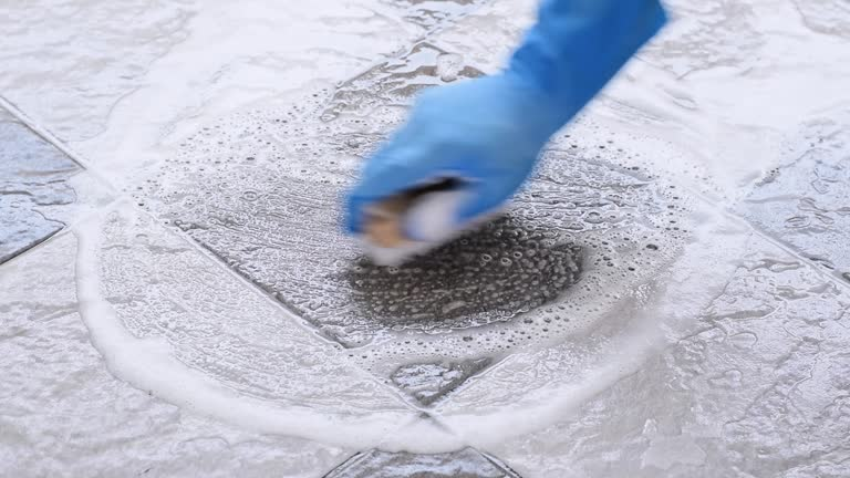 Close-up of hands scrubbing cement patio with a brush during a thorough cleaning process