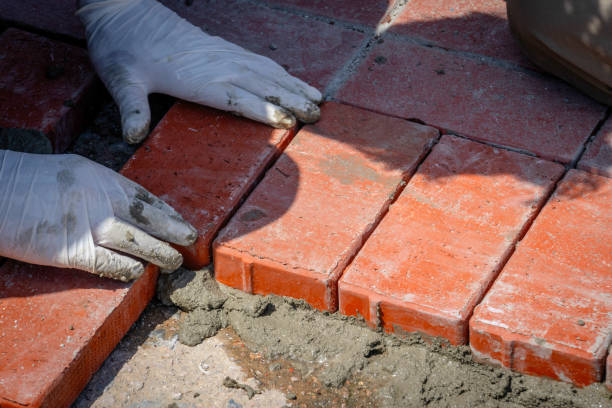 Close-up of hands carefully laying bricks for patio installation in a herringbone pattern