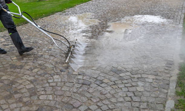 Soapy water being poured over dirty pavers before cleaning