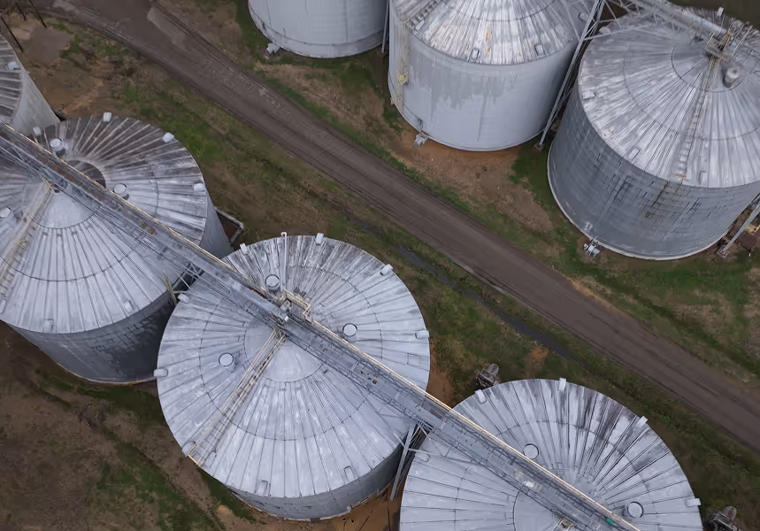 Aerial view of multiple large metal grain silos connected by a conveyor system.