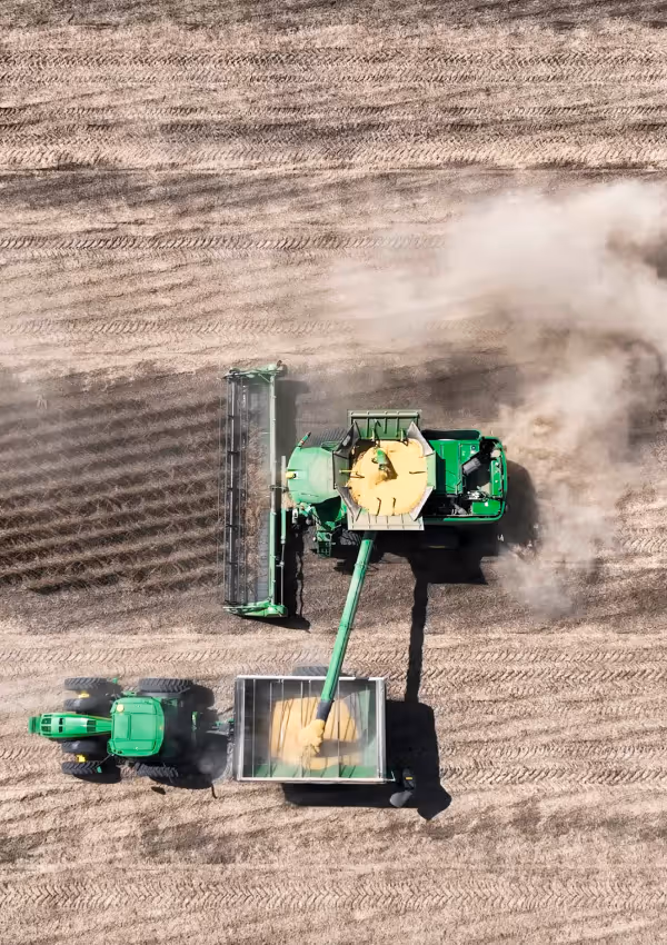Aerial view of a combine unloading harvested grain into a tractor trailer.