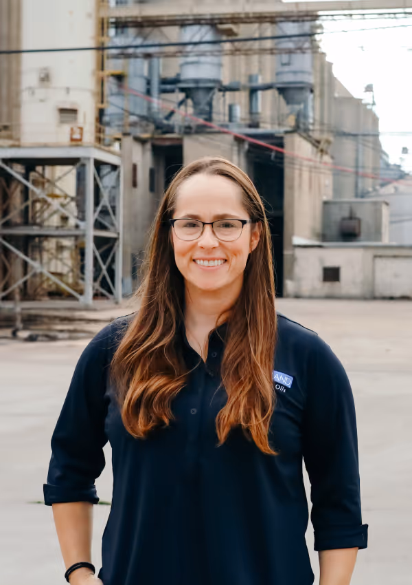 Smiling woman in a Riceland shirt standing in front of a milling facility.