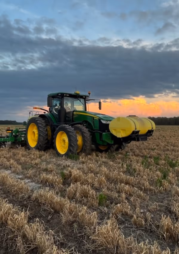 Green and yellow tractor in a harvested field at sunset.