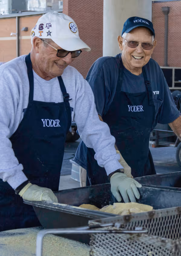 Two men in aprons preparing food at a community cooking event.
