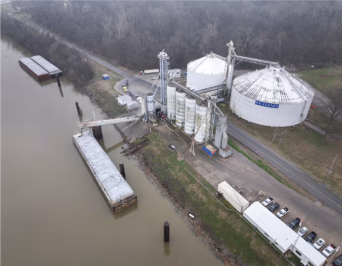 Modern Riceland grain elevator and silos at a riverside port with docked barges.