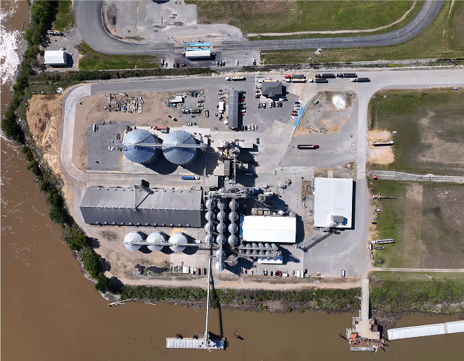 Aerial view of a modern Riceland grain facility with silos and processing buildings near a river.