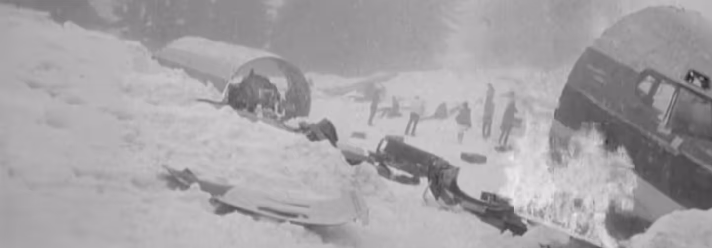 Black and white snowy battlefield with scattered debris and a burning wreckage of a vehicle or aircraft.