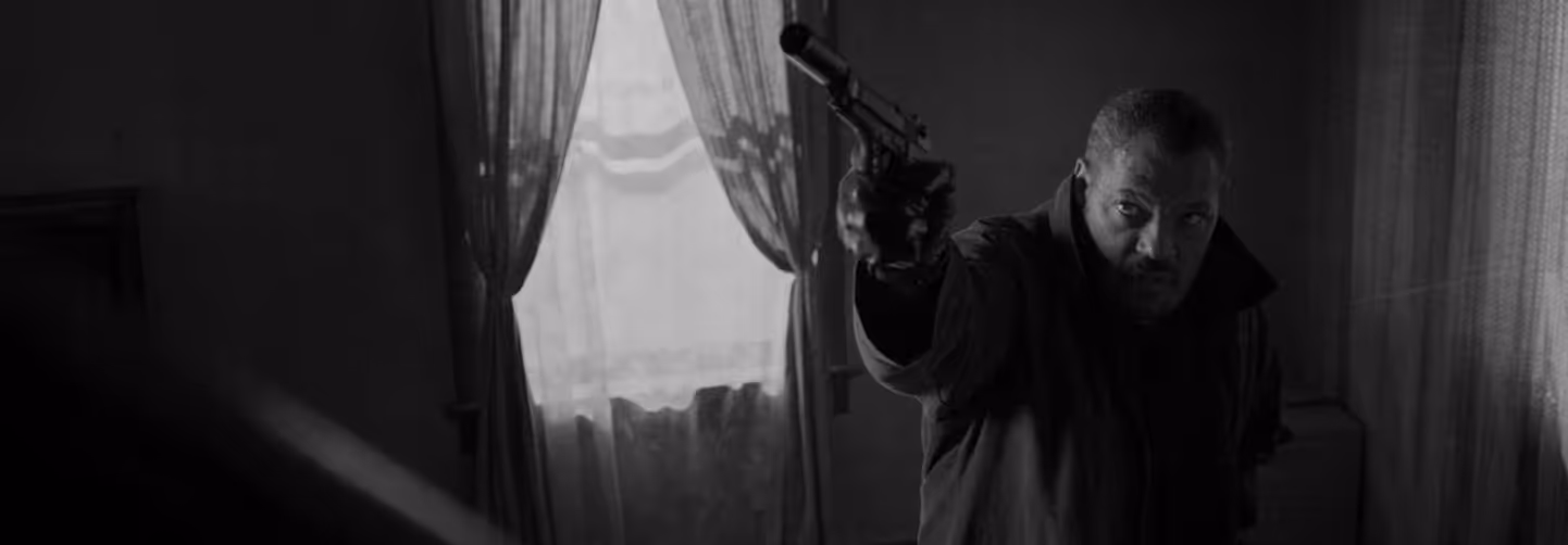 Black-and-white image of a man in a dark coat aiming a pistol inside a dimly lit room with sheer curtains.