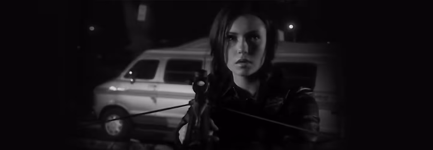Black and white banner image of a person aiming a rifle at night with a van in the background, evoking a suspenseful or dramatic mood.
