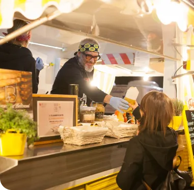 Man with a head band serving food from his yellow food truck