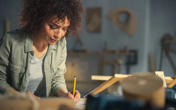 Woman holding a yellow pencil working at an art desk
