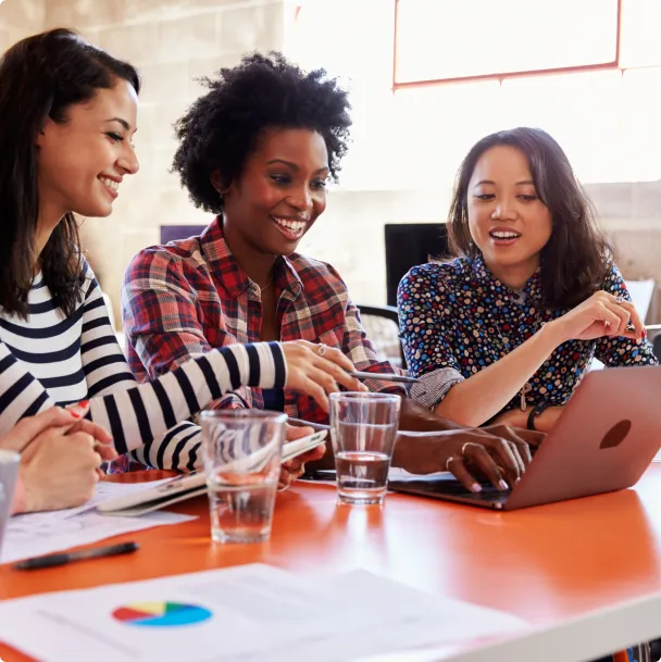 Three woman sitting at an orange table looking at a computer