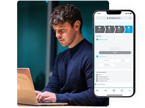 A man in a blue shirt typing on a computer with a phone on the side showing the clicklease application process