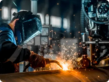 A welder in a large mask working on a large pipe