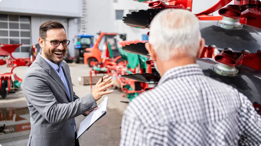 A smiling man with glasses in a business suit showing off equipment to an elderly customer
