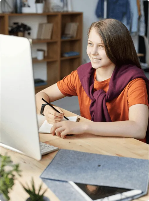 A girl studying on her computer while taking notes on a book