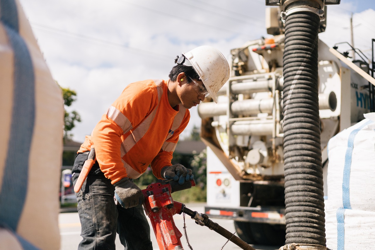 Construction worker in orange safety gear operating heavy equipment outdoors on-site daily.