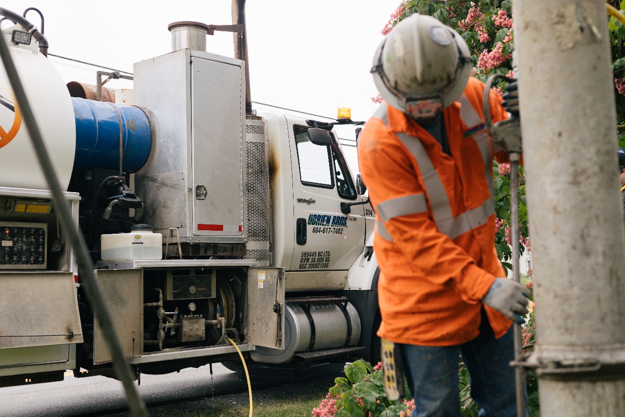 Workers in orange safety gear near large truck and electricity utility pole repair.