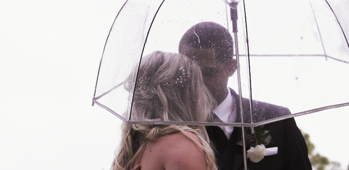 A wedding couple standing in the rain under an umbrella. 