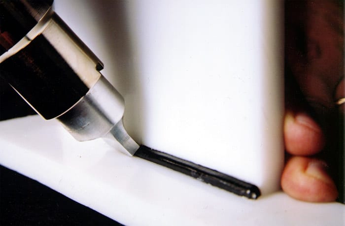 Close-up of a plastic welding torch melting black welding rod onto a white plastic surface.