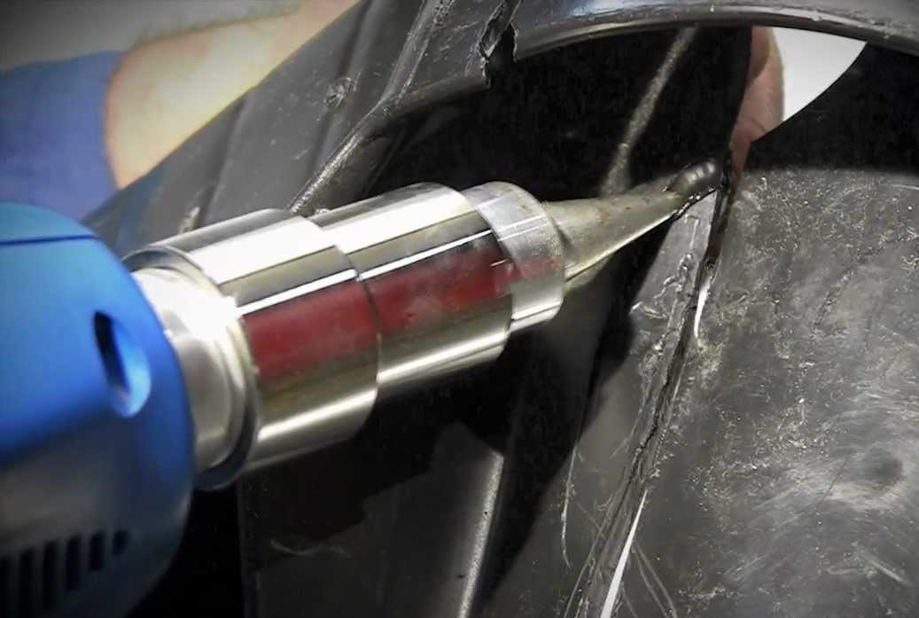 Close-up of a hot air tool applying heat to weld or repair a black plastic surface.