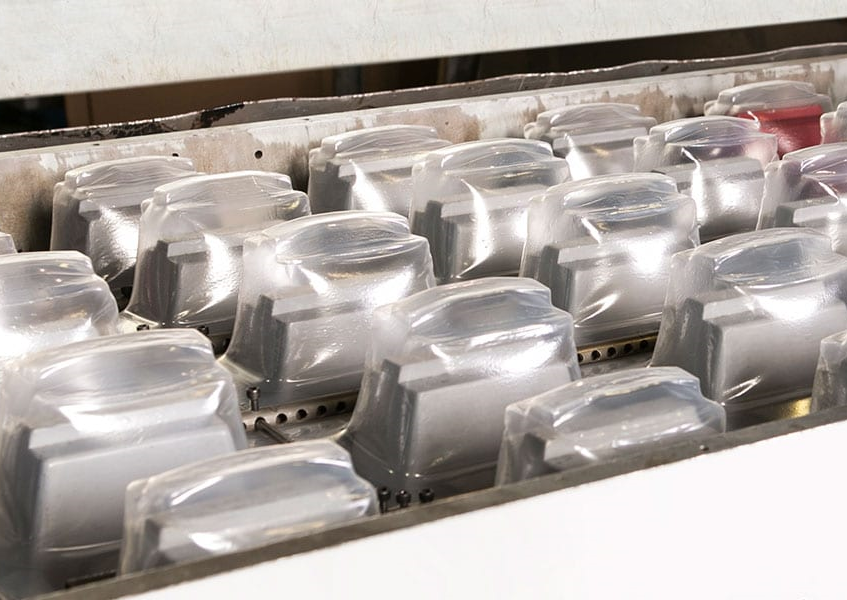 Rows of transparent plastic molds shaped over metallic forms during a vacuum forming process.