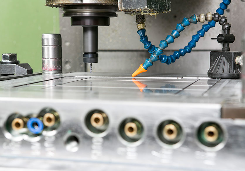 Close-up of a CNC milling machine with a rotating drill bit and coolant nozzles over a metal workpiece.