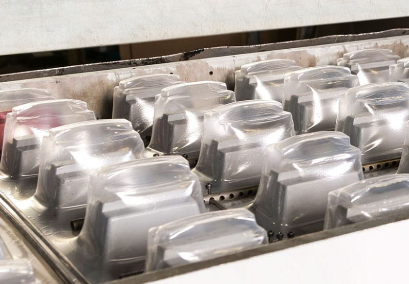 Rows of transparent plastic containers arranged on a metal surface in an industrial setting.
