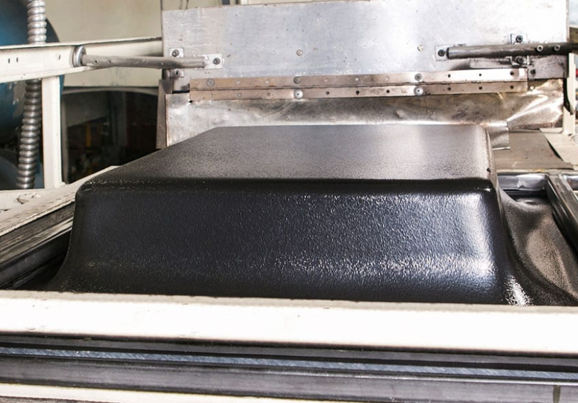 Close-up of a black textured automotive bed liner during the manufacturing process inside a mold press.