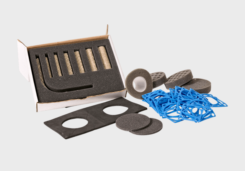 Assorted foam and rubber gaskets, rollers, and blue plastic spacer parts next to a small open box with foam inserts.