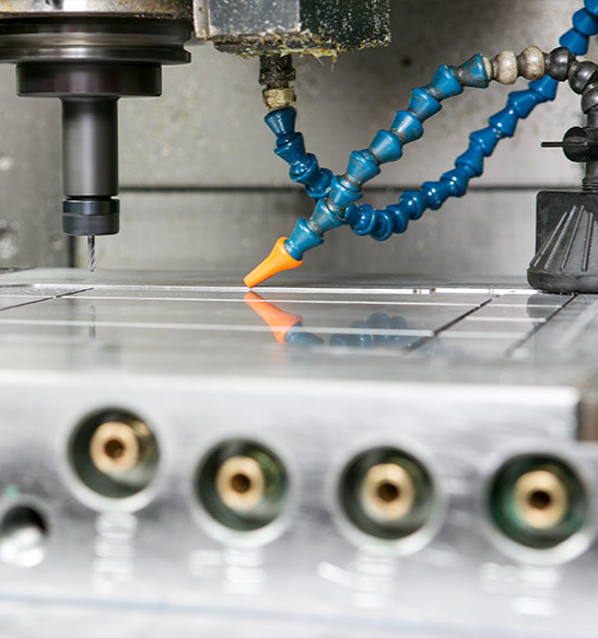 Close-up of a CNC machine drill and a flexible coolant hose with an orange nozzle on a metal work surface.