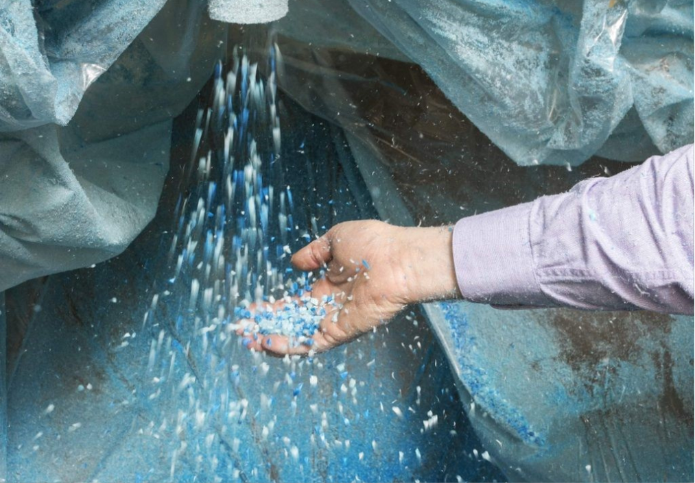 Hand catching small blue and white plastic pellets pouring down inside a container with blue plastic lining.