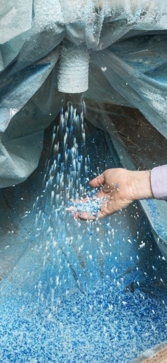 Hand catching small blue and white plastic pellets falling from a chute into a large container.