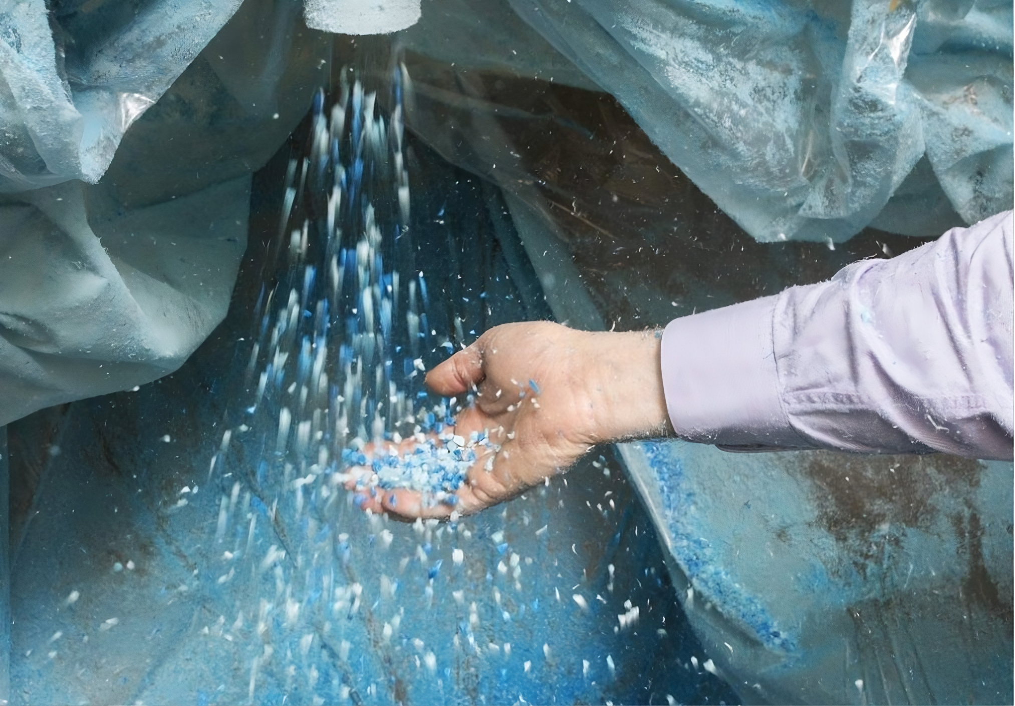 Hand catching falling blue and white plastic pellets inside a large container.