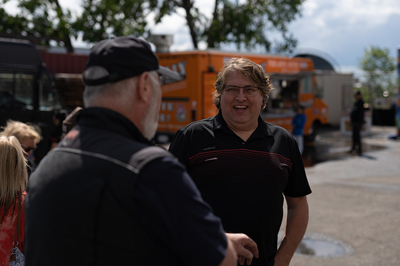 Two men smiling and talking outdoors near a bright orange food truck.