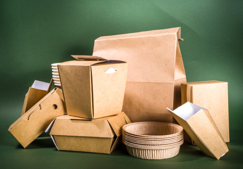 Various eco-friendly brown paper food containers and disposable bowls arranged against a green background.