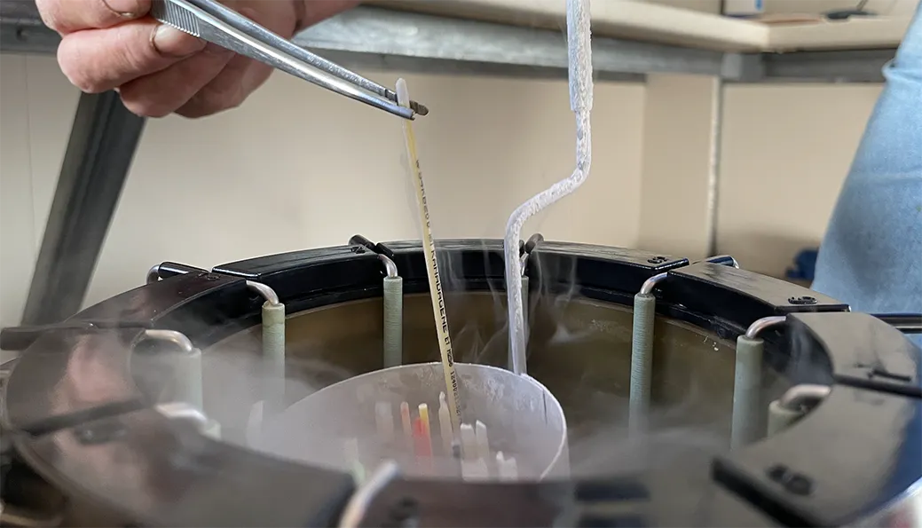 Hand using tweezers to place a small vial into a cryogenic storage container surrounded by vapor.
