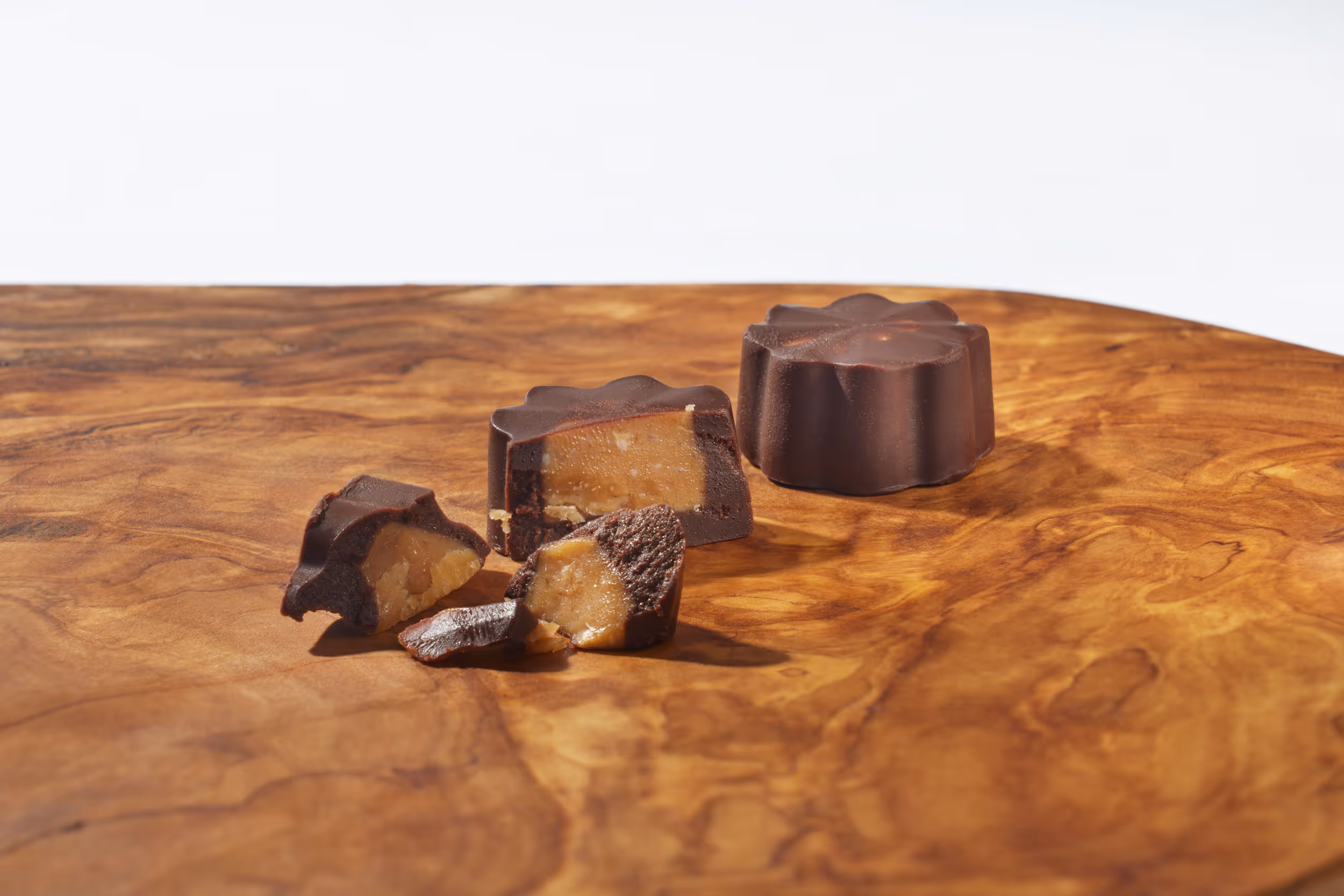 Close-up of flower-shaped dark chocolates with a caramel filling, one whole and others cut open, displayed on a wooden surface.